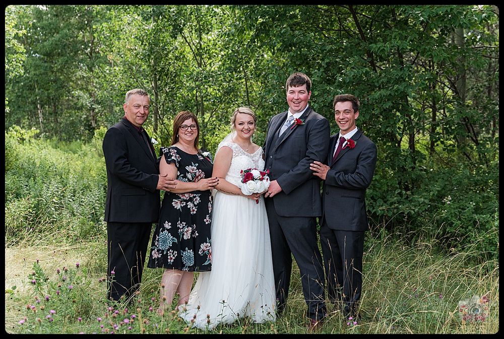 A small wedding party poses for a formal photo outdoors against a lush green background.