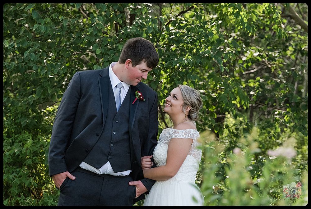 Elegant couple shares intimate moment in formal attire against green foliage.