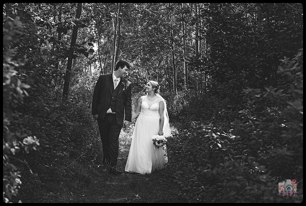 Black and white wedding photograph of couple walking through wooded forest path.