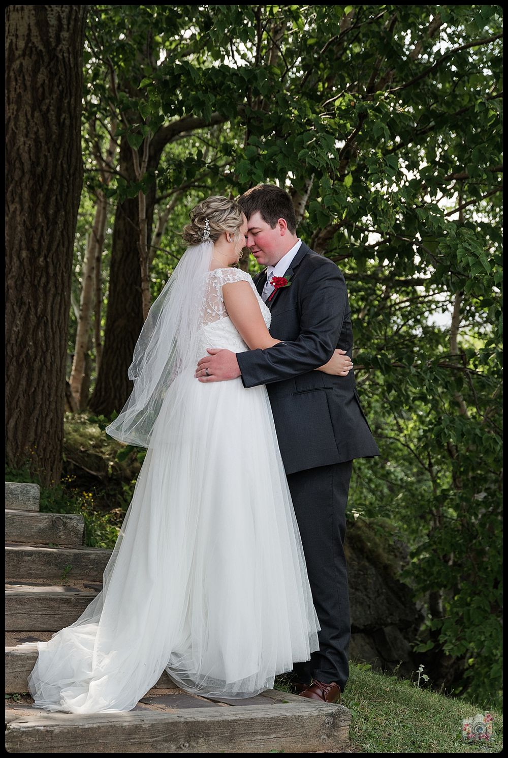 A romantic wedding moment captured on stone steps surrounded by lush greenery and trees.