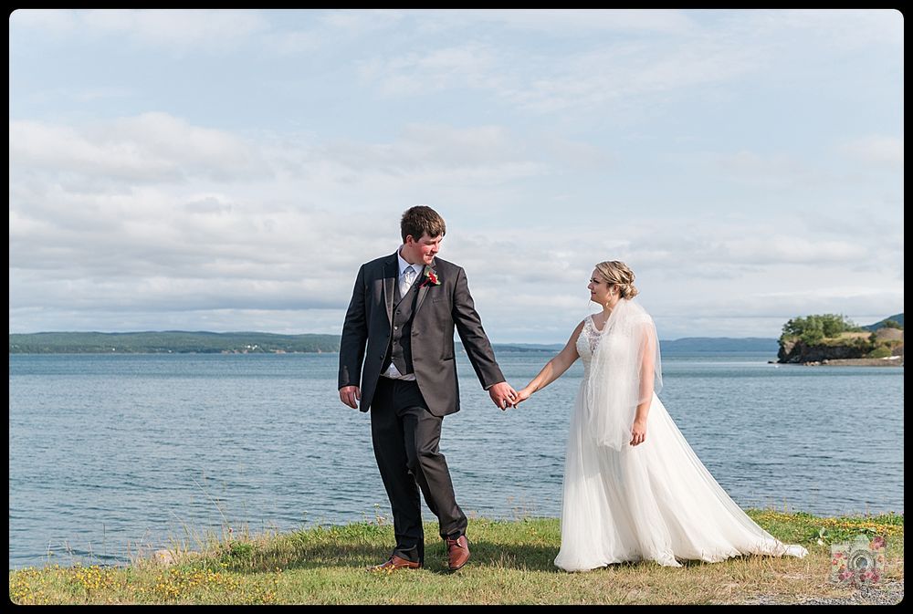 Elegant wedding portrait with couple standing on a seaside cliff against a waterfront backdrop.