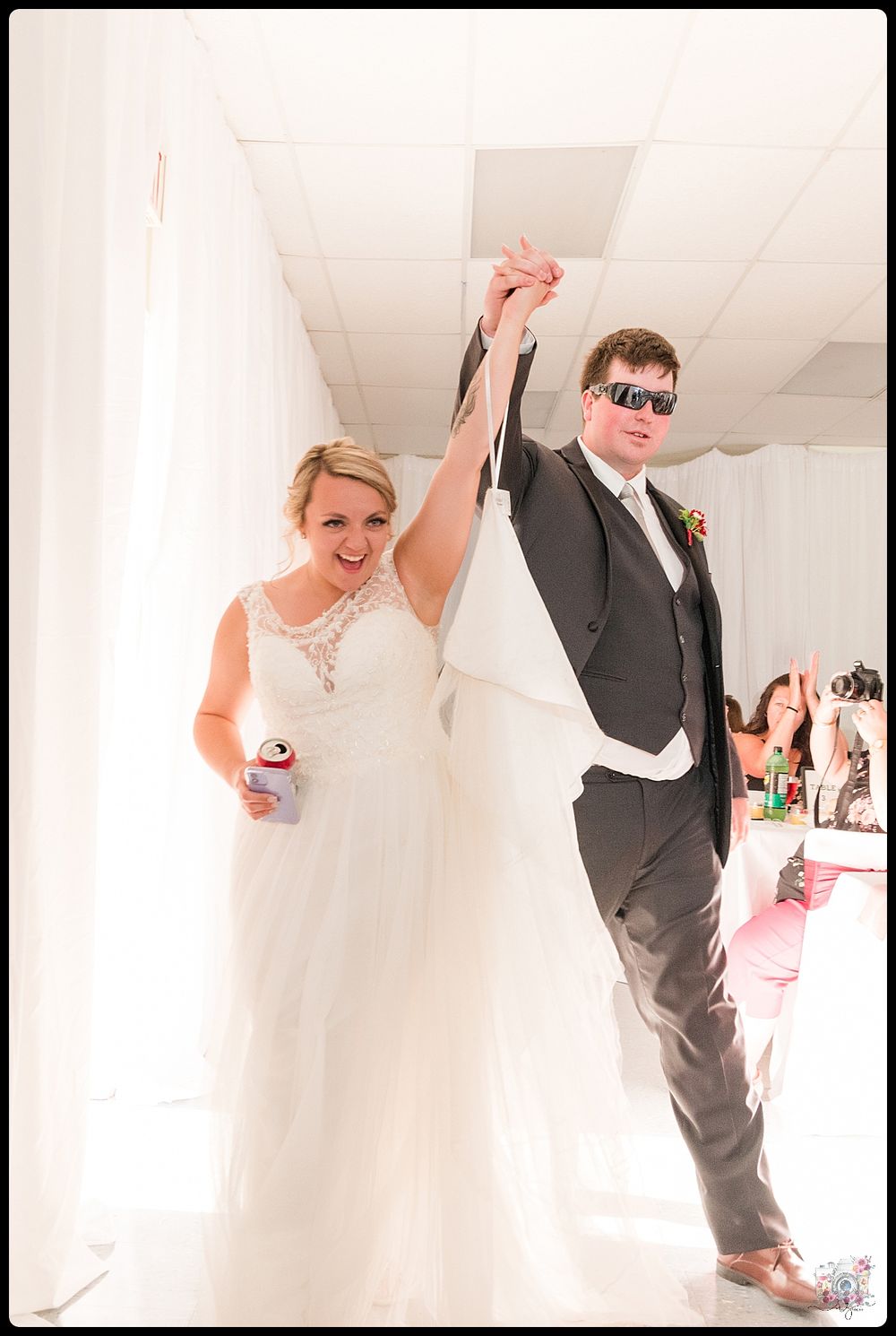 Celebratory moment at wedding reception with couple striking victorious pose in sunlit hallway.