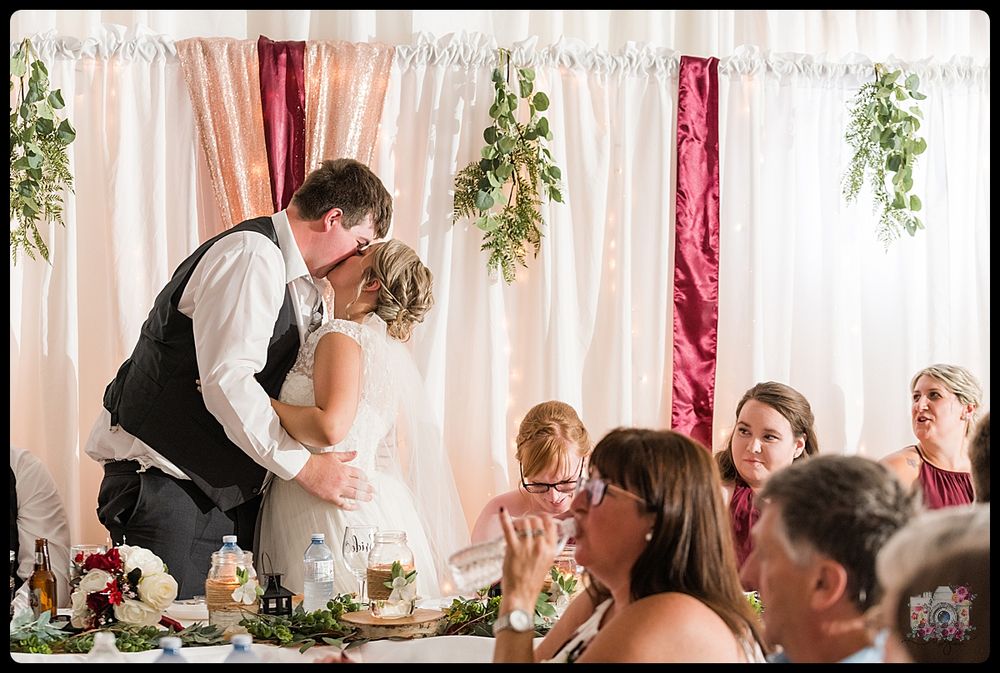 Intimate wedding reception moment with couple sharing a kiss at decorated banquet table.