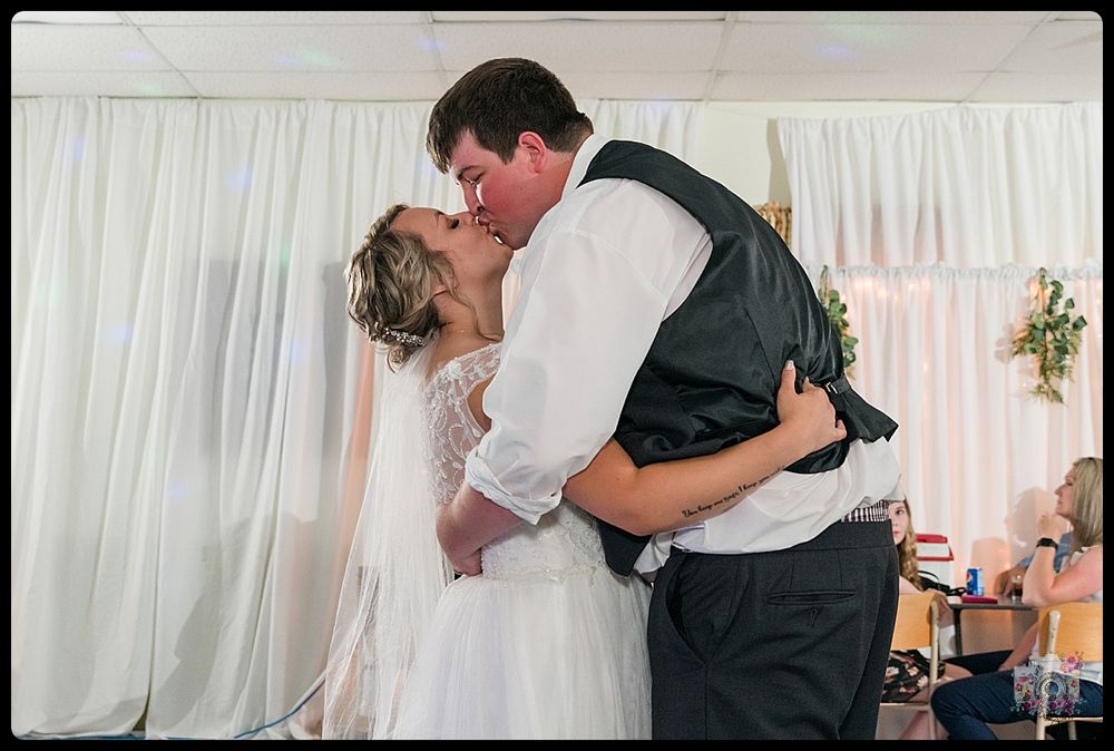A romantic moment between newlyweds sharing their first dance at a wedding reception with white drapes in background.