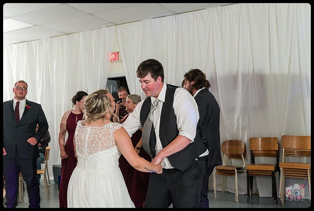 Festive dance moment at wedding reception with guests and white draped walls.