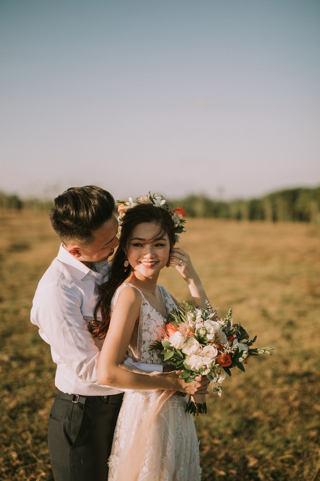 A tender moment captured during a wedding photoshoot in a sunlit meadow.