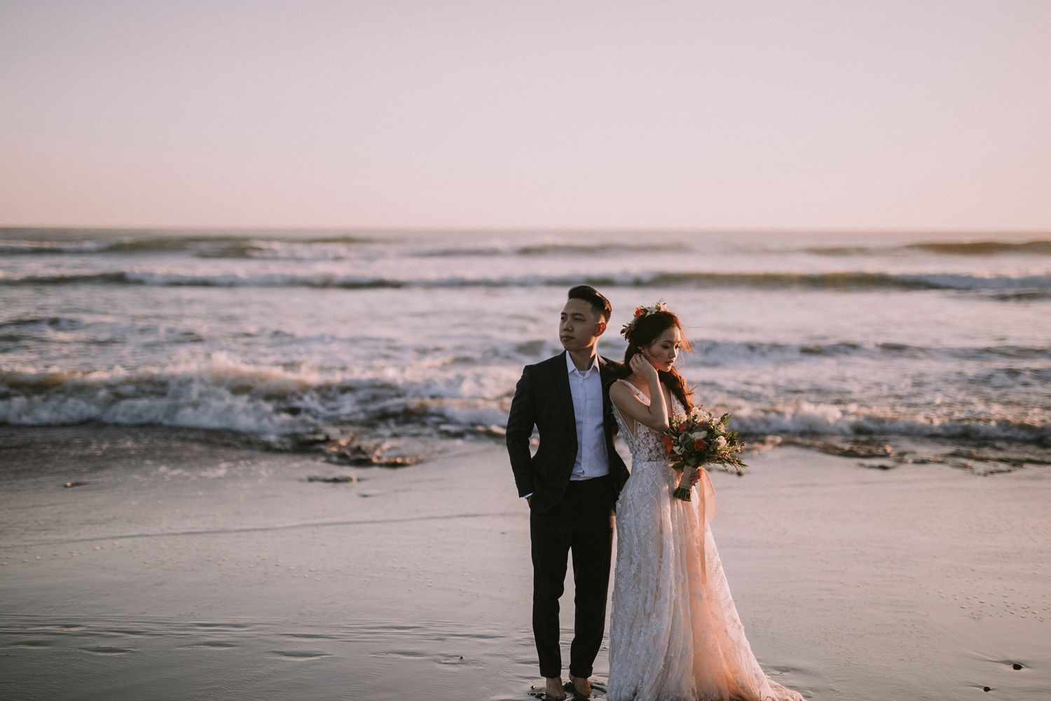 Elegant beachside wedding photography with waves and sunset in the background.