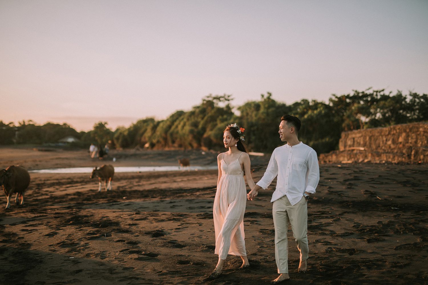 Wedding couple strolling along a dark sandy beach during sunset.