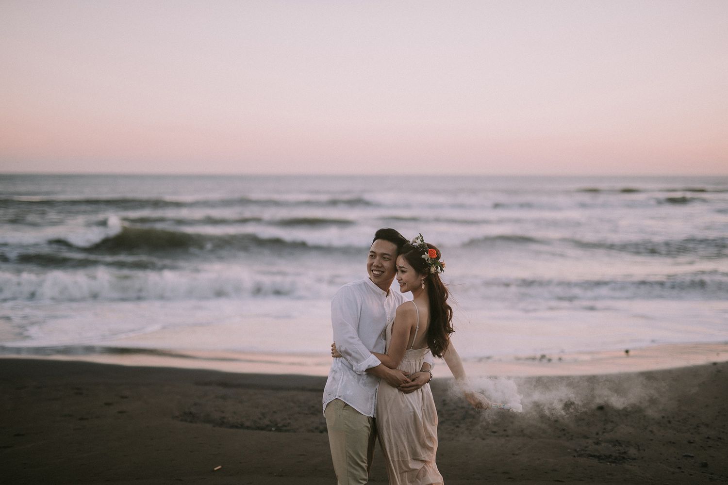 Couple shares an intimate moment on a beach during golden hour with ocean waves behind them.