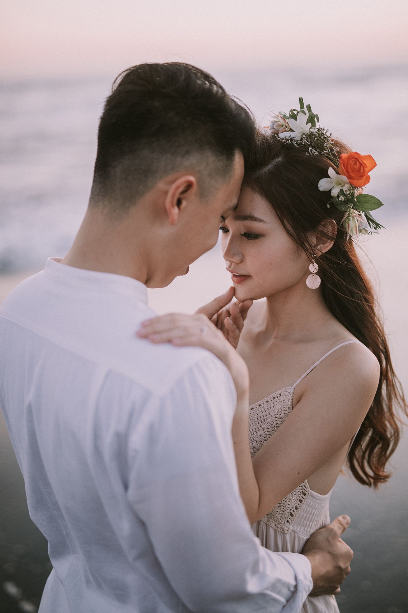 Close-up of couple in wedding attire sharing tender moment against ocean backdrop.