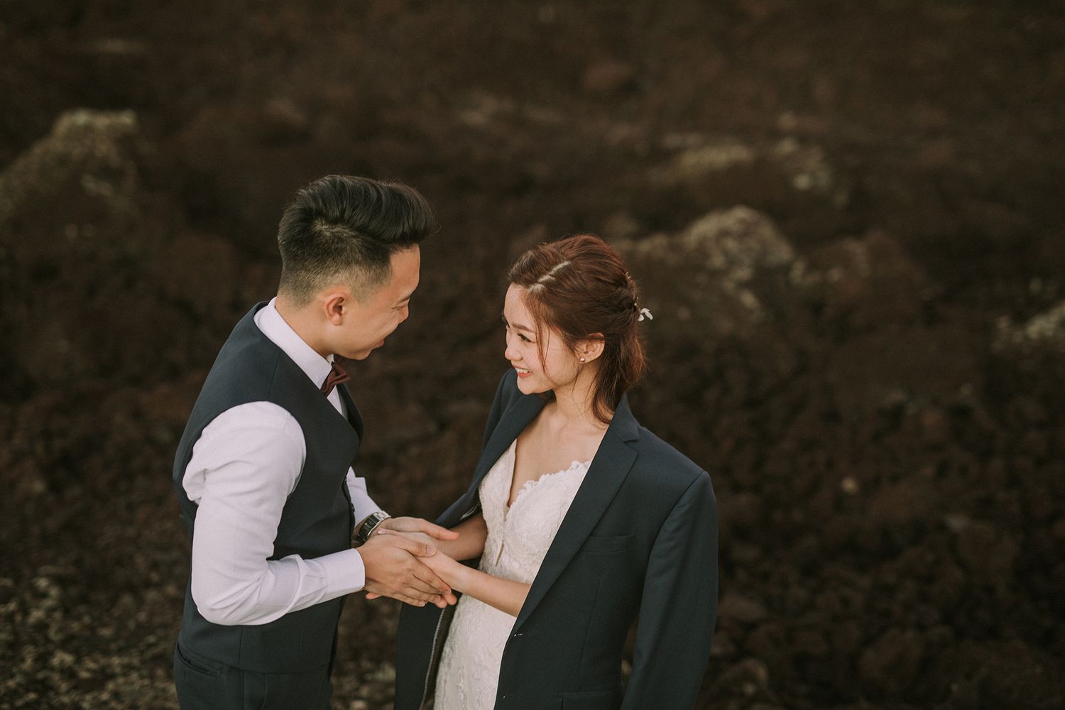 Couple in formal attire poses against dramatic rocky landscape.