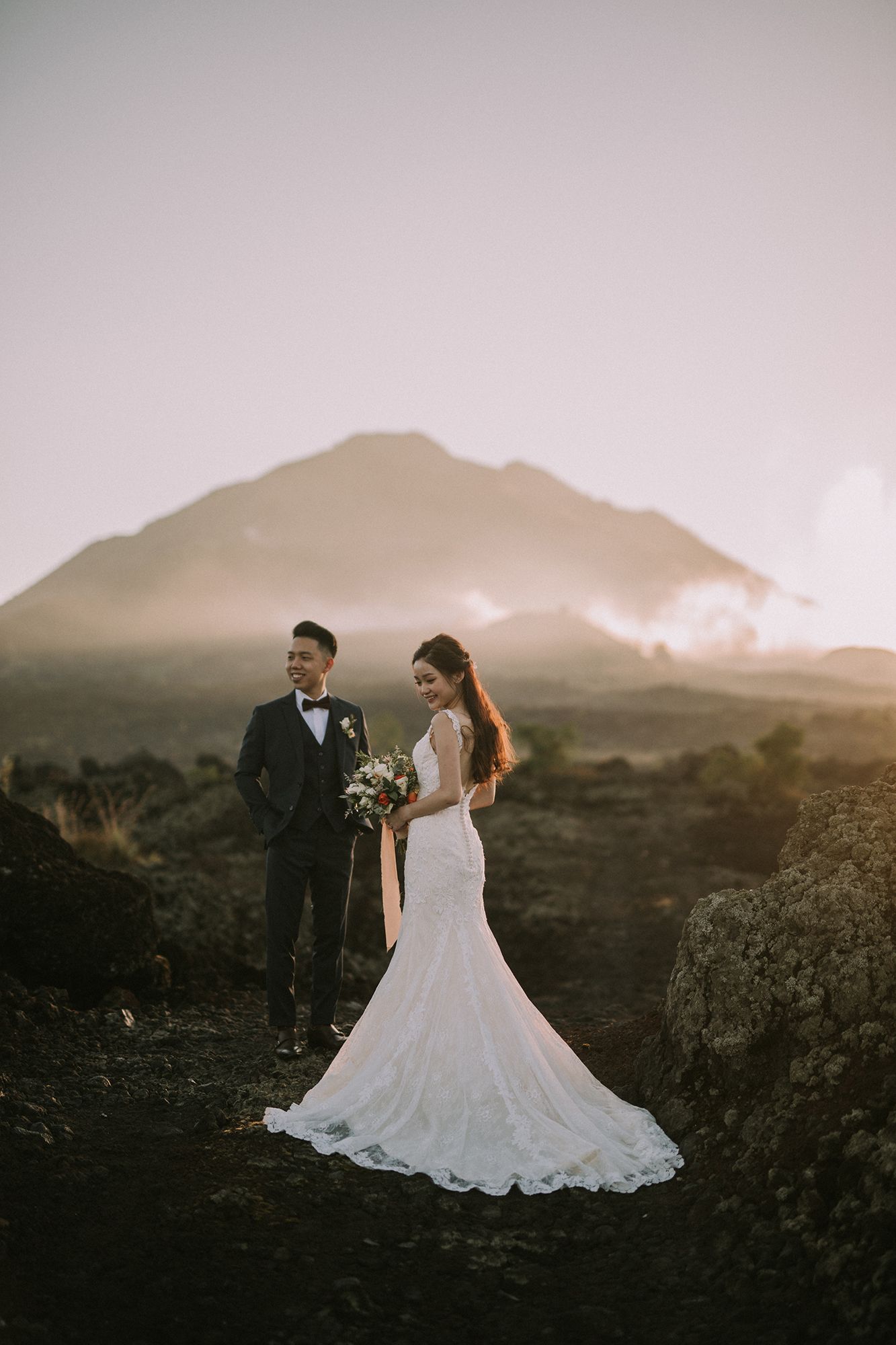 Elegant wedding dress flows against dramatic mountain landscape at dusk.