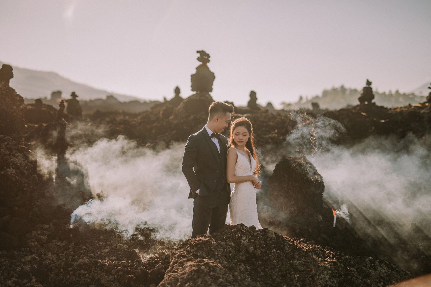 Newlyweds pose among misty volcanic rocks during sunset photoshoot.