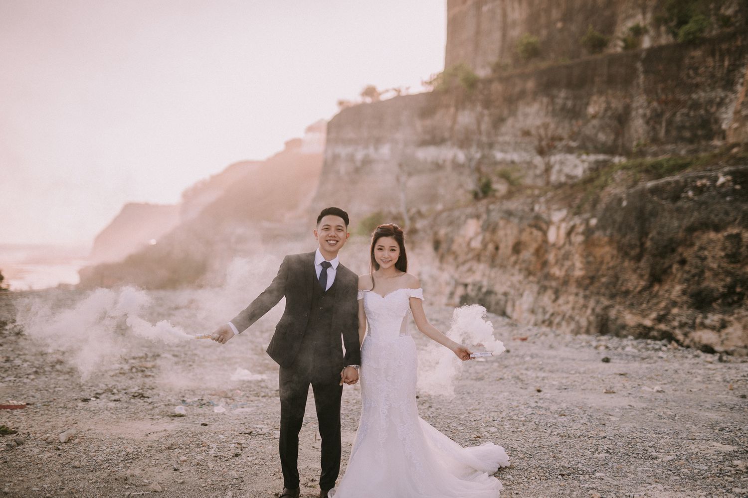 Newlyweds walking along a rocky beach path during golden hour.