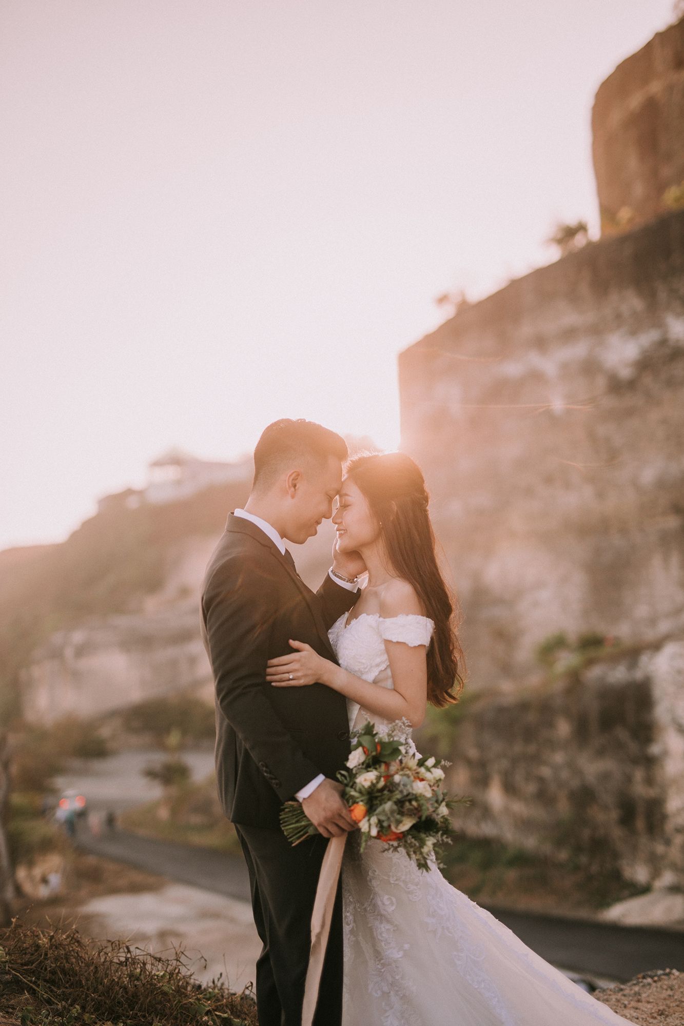 Romantic wedding couple sharing a tender moment against dramatic cliffs at sunset.