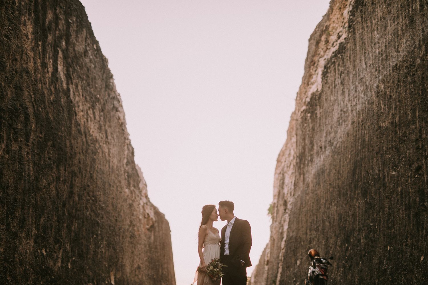 Silhouetted couple embracing against towering coastal cliff walls.