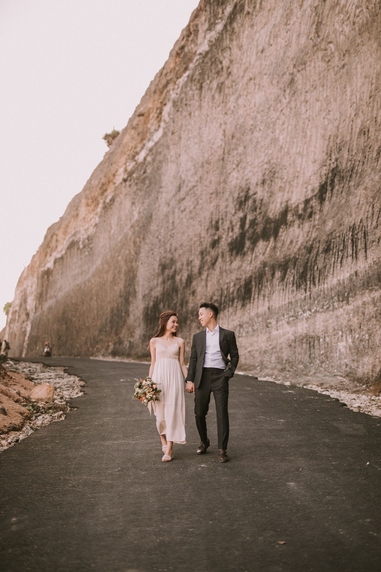 Elegant couple strolling along black sand beach with dramatic cliff backdrop.