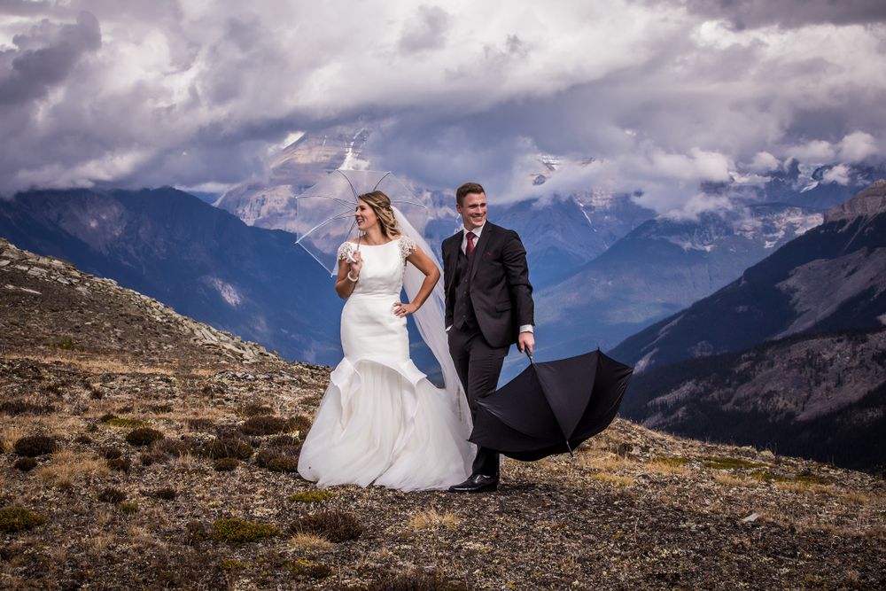 Couple poses dramatically against stunning mountain backdrop with dramatic cloudy skies.