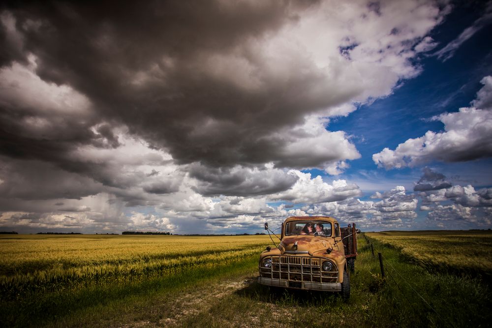 Old rustic truck in golden wheat field under dramatic cloudy sky.