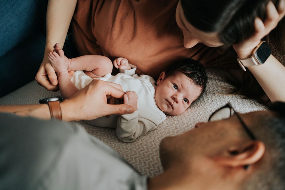 noworodek, mama i tata leżą na łóżku - sesja noworodkowa Kraków
