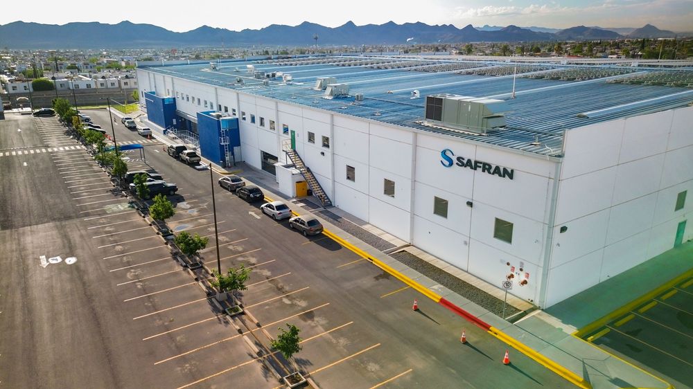 Panoramic aerial view of industrial buildings and solar panel arrays with mountains in the background.