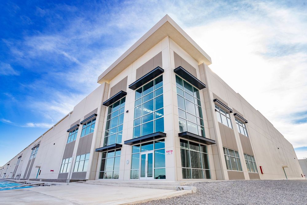 Modern industrial warehouse building with large glass windows and beige facade under a blue sky.