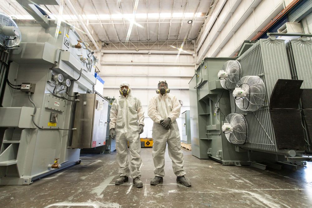 Workers in protective hazmat suits clean and disinfect an industrial facility with specialized equipment.