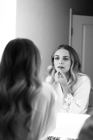 Black and white portrait of bridesmaid getting ready by putting on lipstick