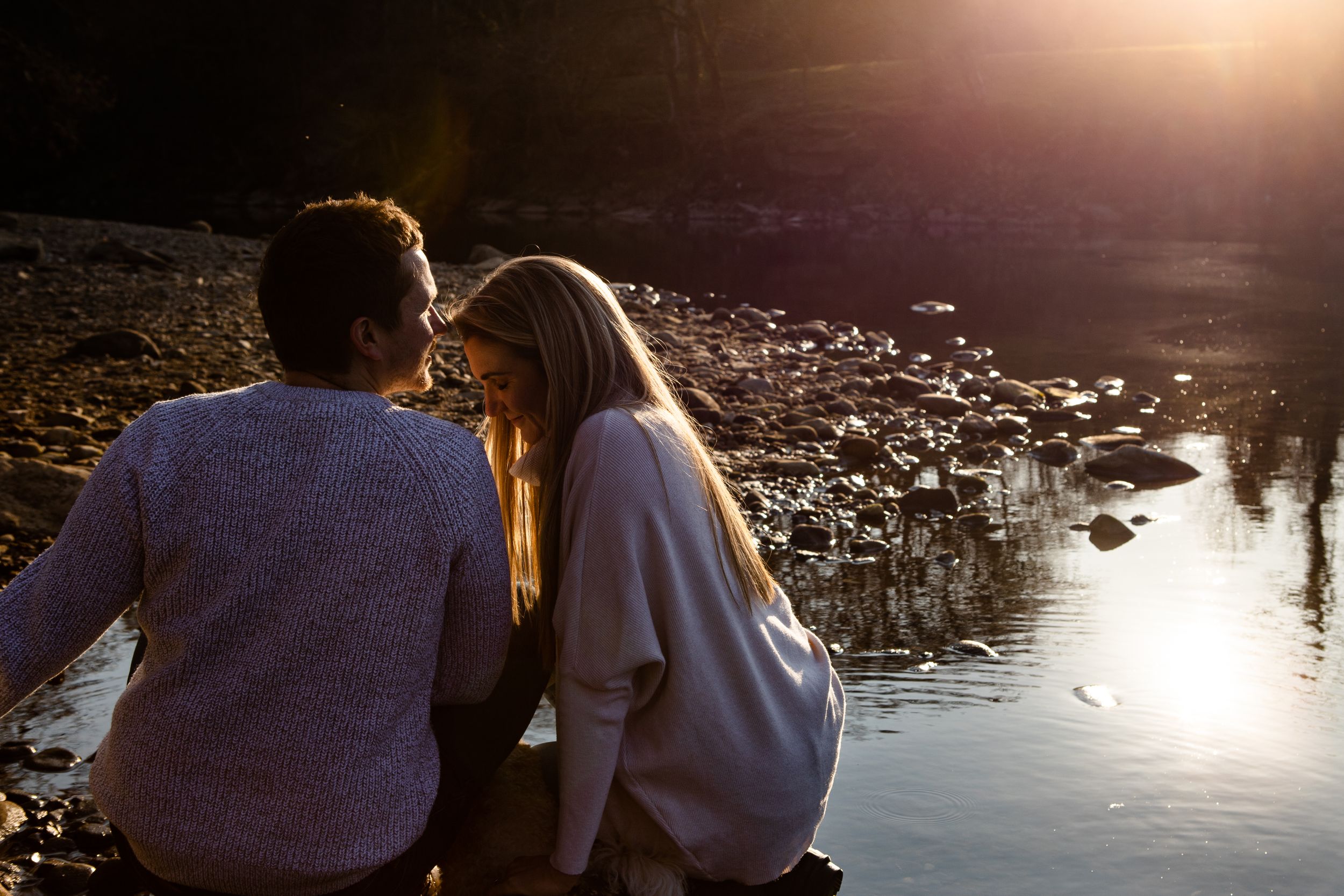 "couple kissing sitting by river sunset"