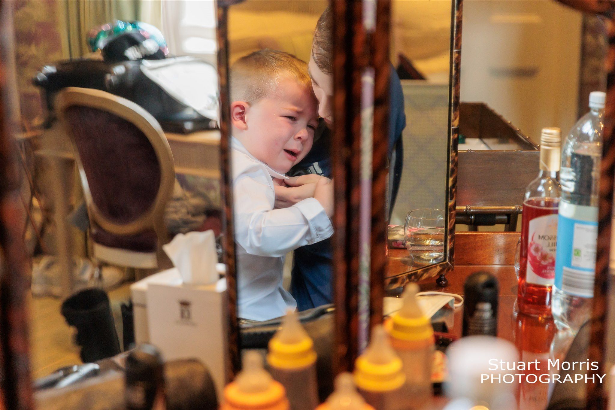 Young boy crying held by his day reflected in a mirror on the wedding morning. Knowsley hall wedding photographer