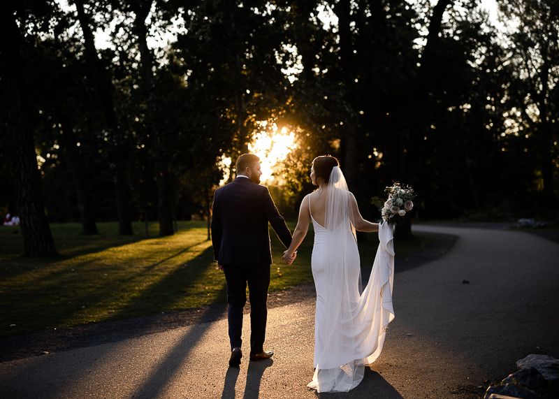 Wedding couple silhouetted against setting sun on tree-lined pathway.