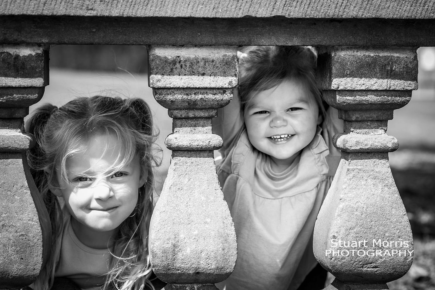 2 little girls peep through the stone balustrade in the gardens at Walton hall. Stuart Morris Photography