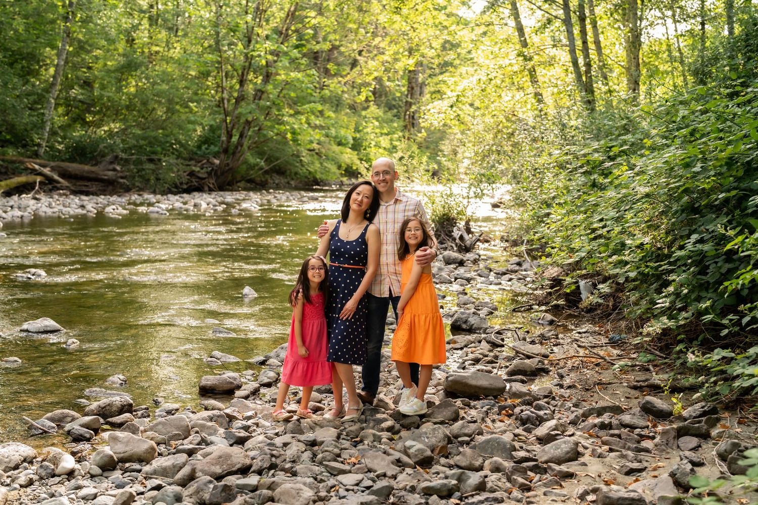 People exploring a rocky creek bed surrounded by lush green forest on a sunny day.