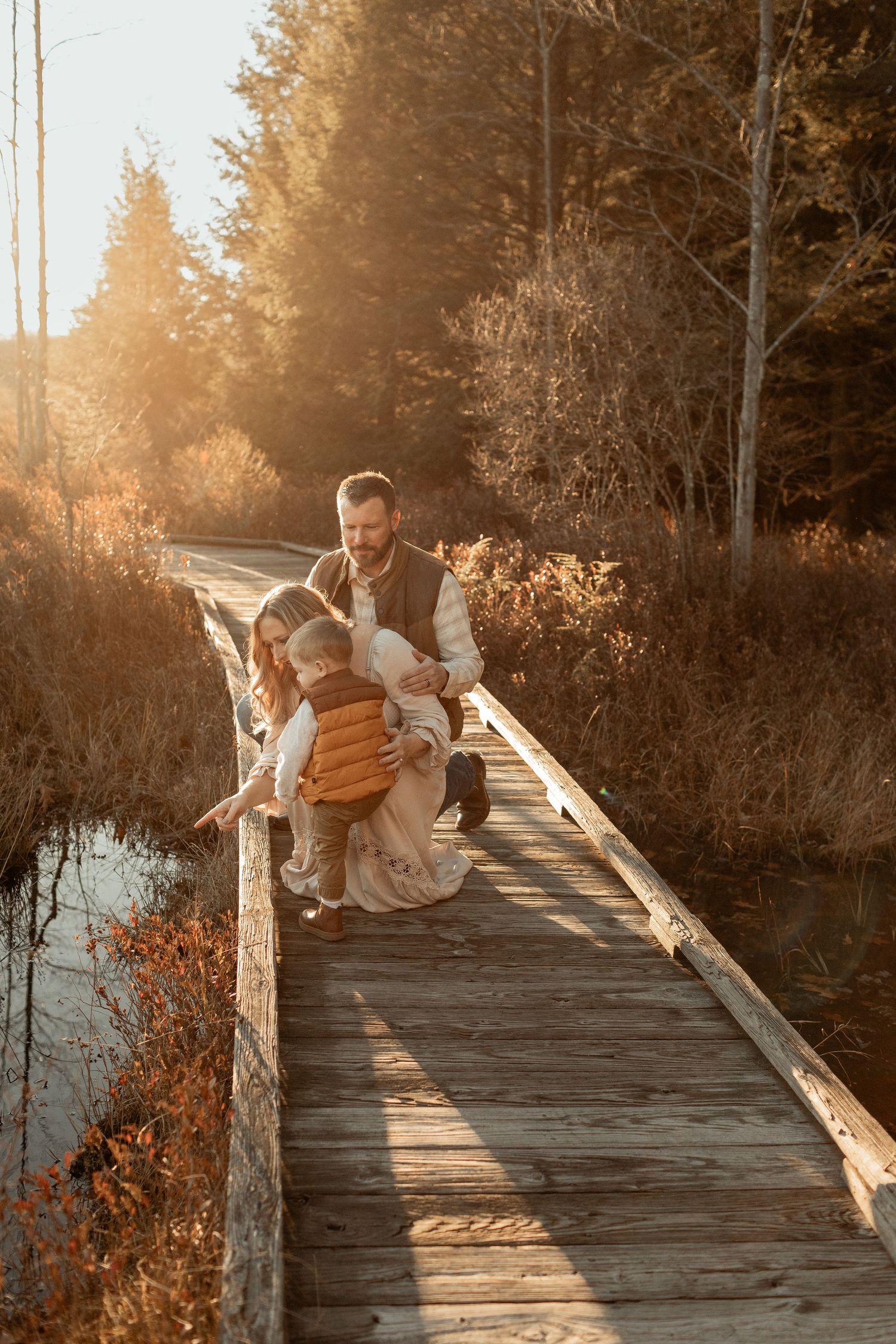 Family sharing intimate moment on wooden bridge during golden hour.