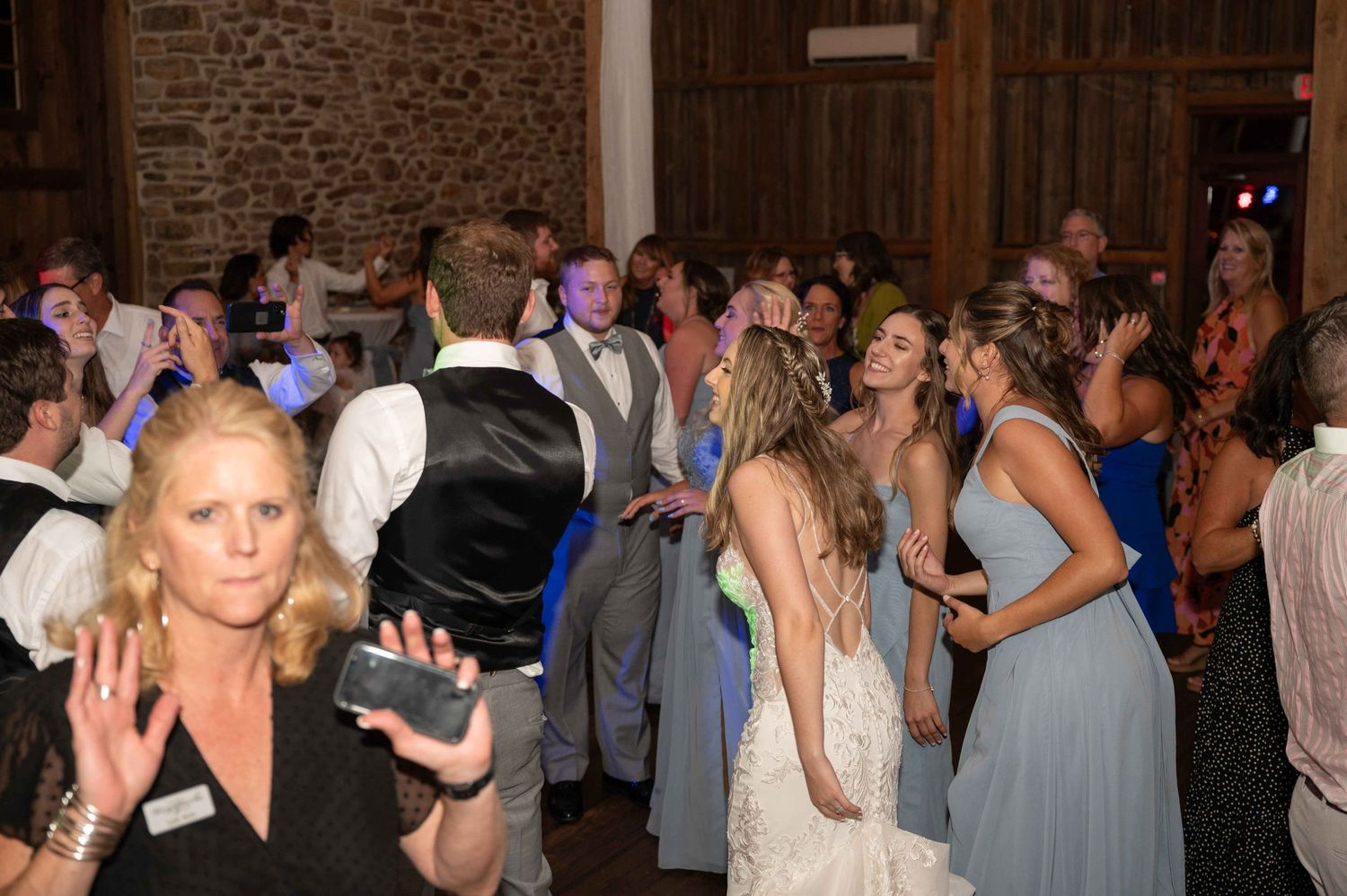 Wedding guests dancing and celebrating on a crowded dance floor in a rustic barn venue.