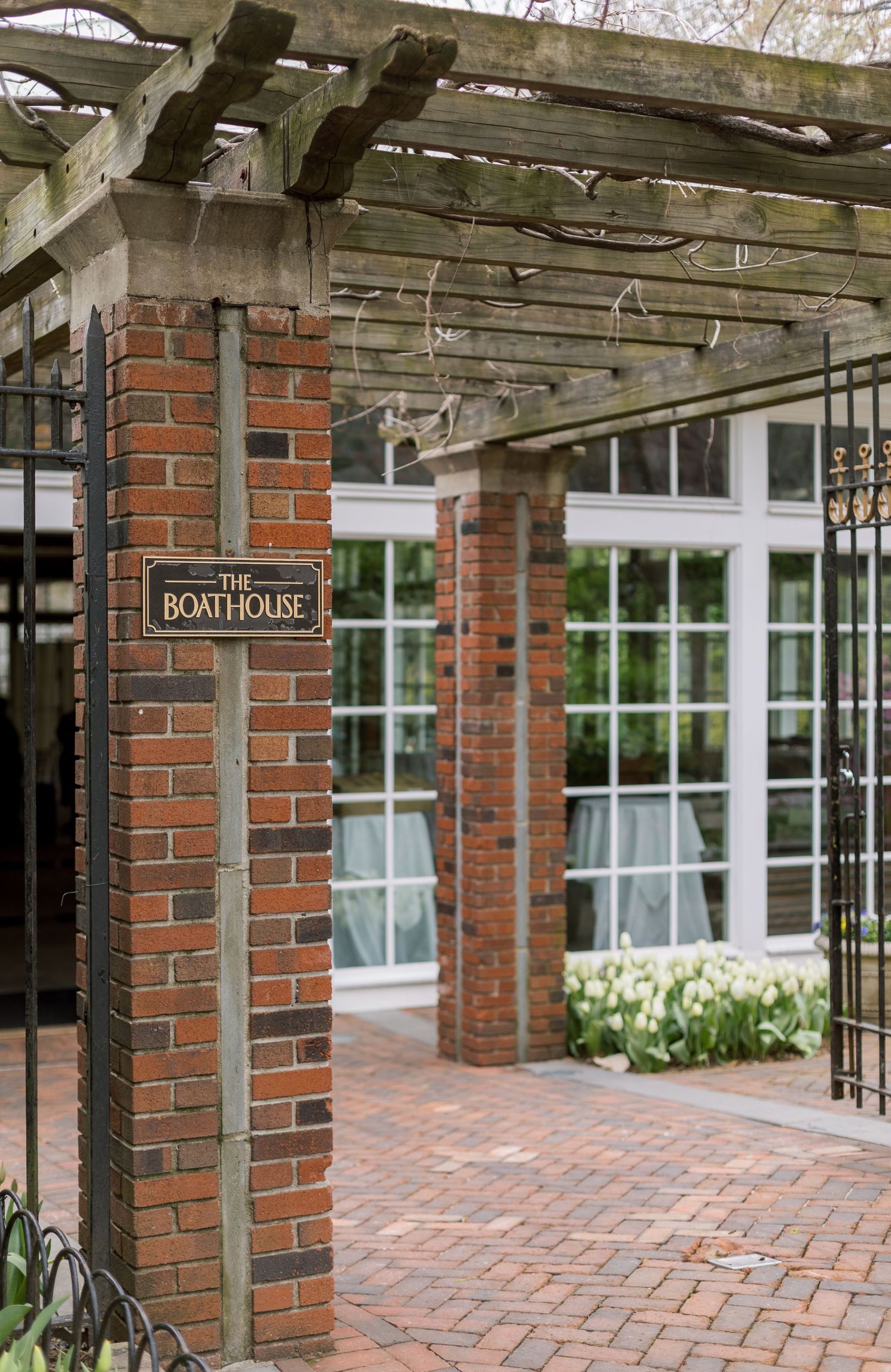 Brick entrance to The Boathouse with wooden pergola and brick paved walkway.