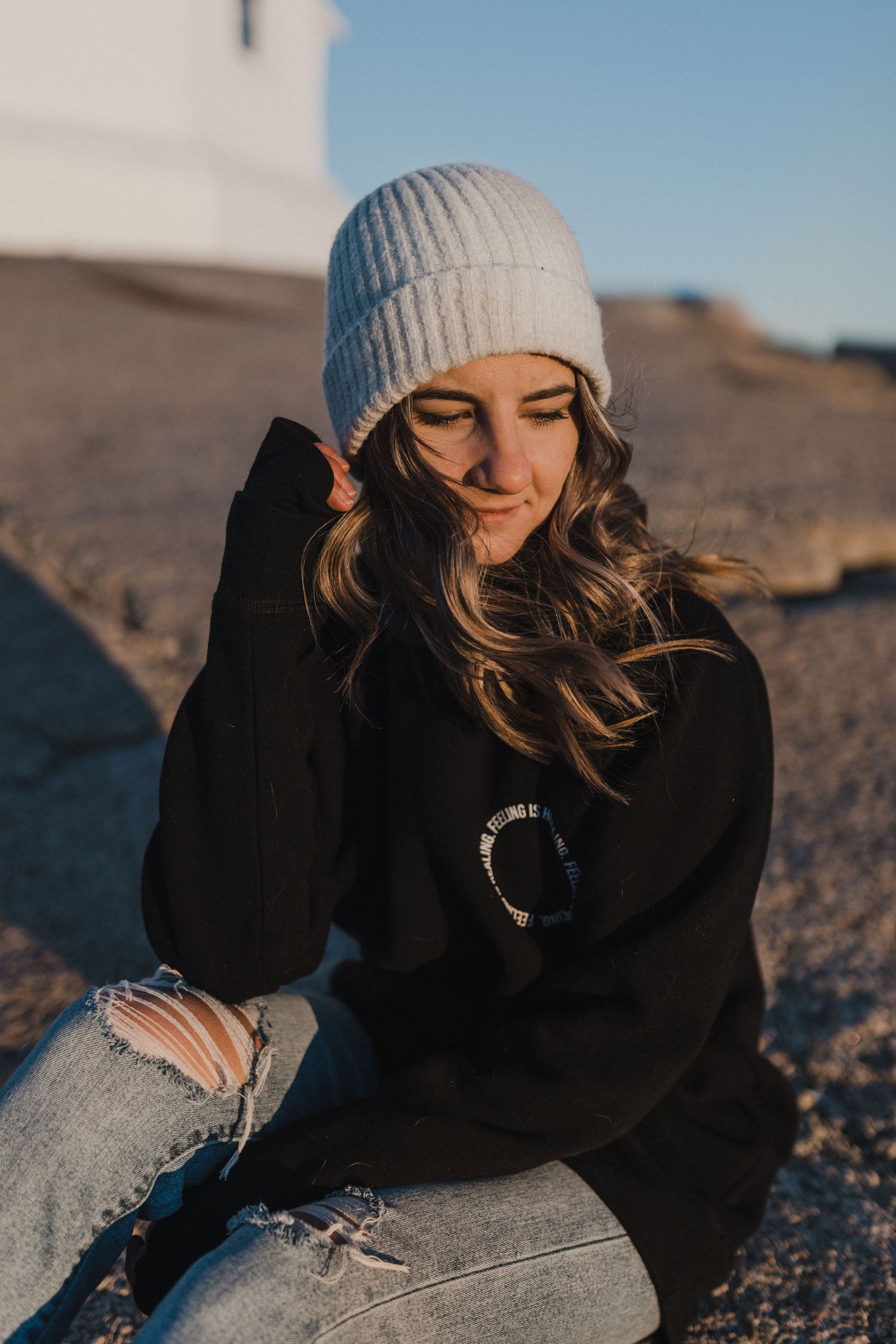 A portrait of Charlotte Buckle Photography in front of Peggy's Cove Lighthouse wearing a Feeling is Healing sweater.