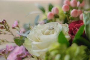 A diamond engagement ring rests elegantly among white roses and pink flowers in a bridal bouquet.