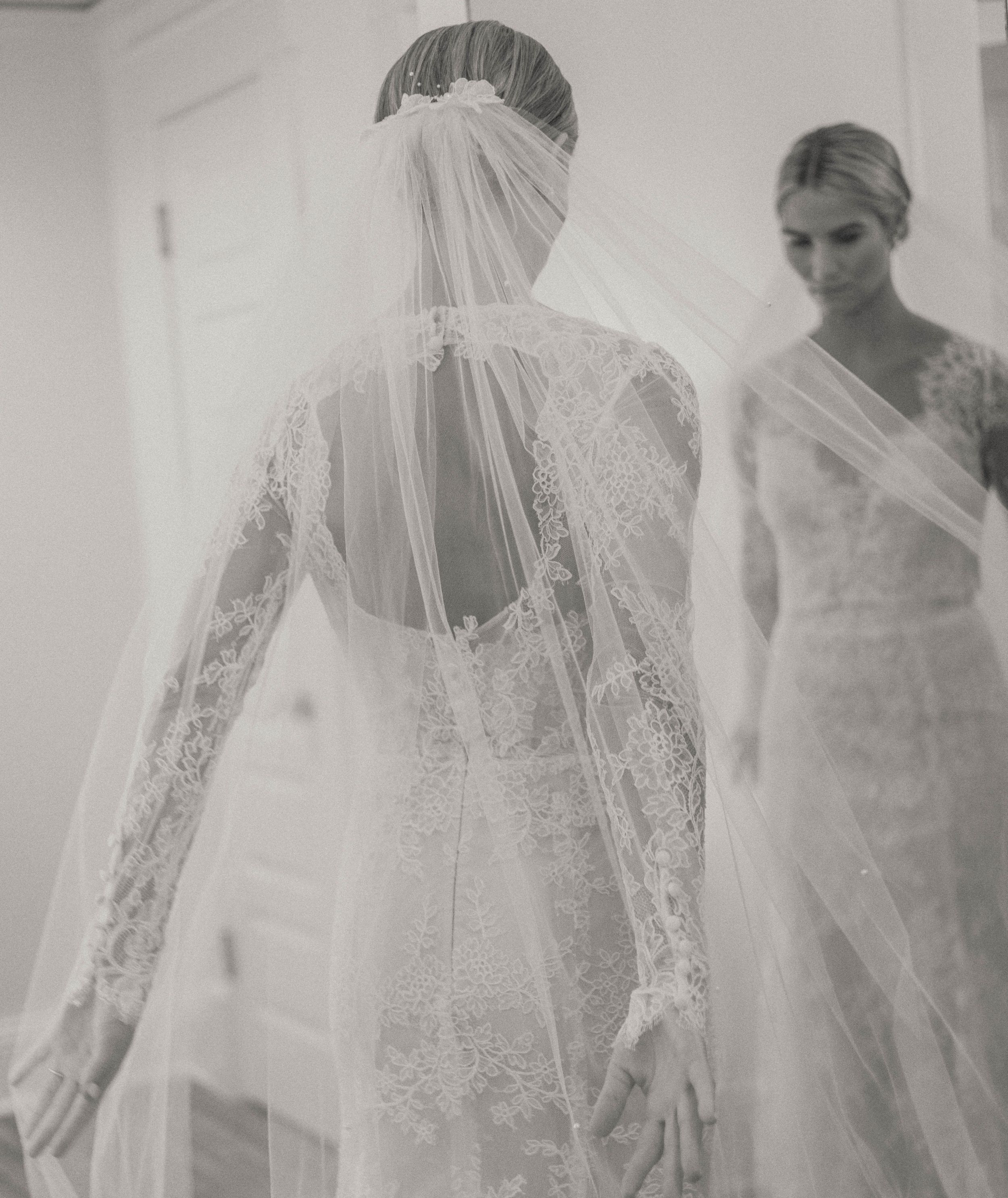 Black and white photo of a bride in lace wedding gown and veil reflected in a mirror.