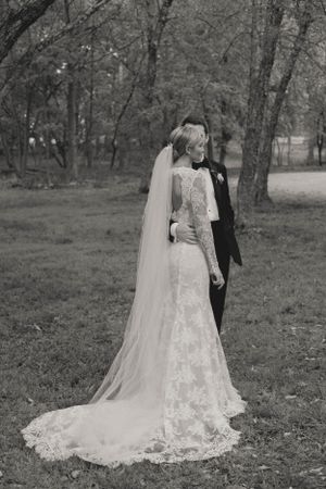 Black and white portrait of bride and groom standing together in a tree-lined garden setting.