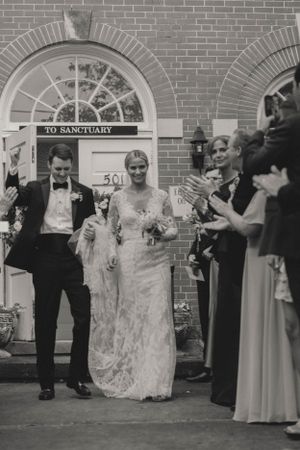 Black and white photo of newlyweds exiting church greeted by cheering guests after ceremony.