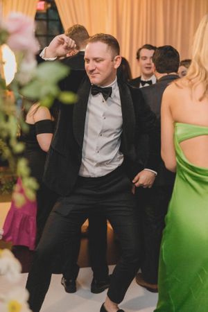 Energetic wedding guest in black tuxedo dancing enthusiastically on the reception dance floor.