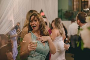 Excited wedding guest in sage green dress holding champagne glass on lively reception dance floor.