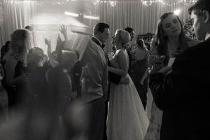 Black and white photo of bride and groom sharing first dance surrounded by celebrating guests.