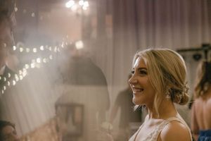 Smiling blonde bride with updo hairstyle at elegant wedding reception with warm string lights.