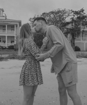 Black and white photo of couple sharing a romantic kiss outdoors near historic beach houses.