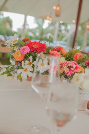 Colorful wedding centerpiece with pink zinnias, ranunculus, and white cosmos on reception table.