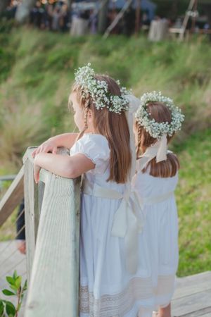Two flower girls in white dresses with baby's breath floral crowns standing on wooden steps.