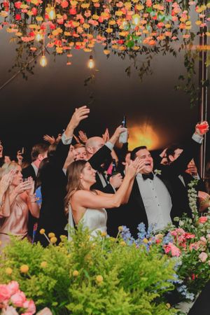 Bride and groom dancing under colorful floral ceiling installation at vibrant wedding reception.