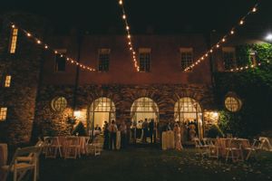 Outdoor wedding reception at night with string lights adorning a historic stone venue.